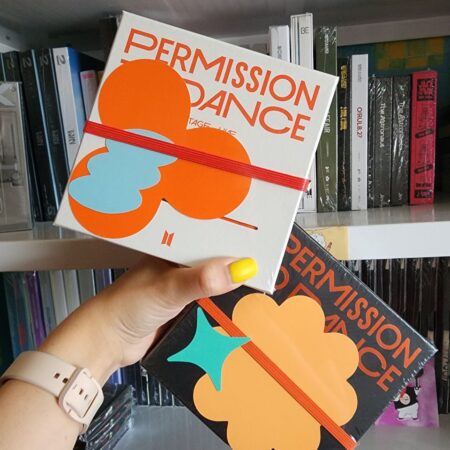 Два видання BTS «Permission to Dance On Stage Live» — біле та чорне — на тлі полиці з K-pop альбомами