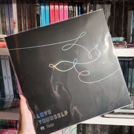 Альбом BTS «Love Yourself 轉 Tear» у чорній обкладинці з голографічним логотипом на тлі полиці з K-pop альбомами