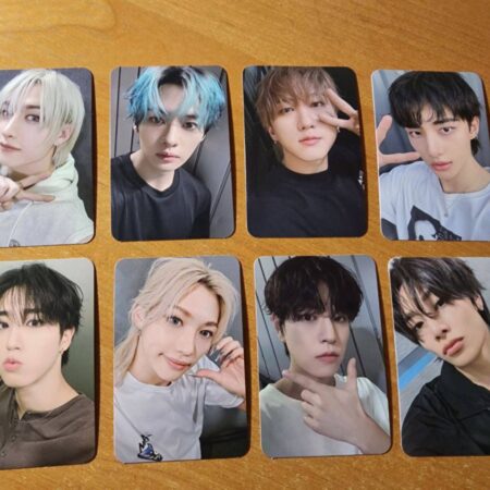 Вісім K-pop фотокарток із портретами молодих чоловіків, розкладених на дерев'яній поверхні
