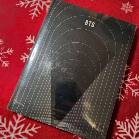 Альбом BTS із темною обкладинкою з концентричними арками на червоному святковому тлі зі сніжинками